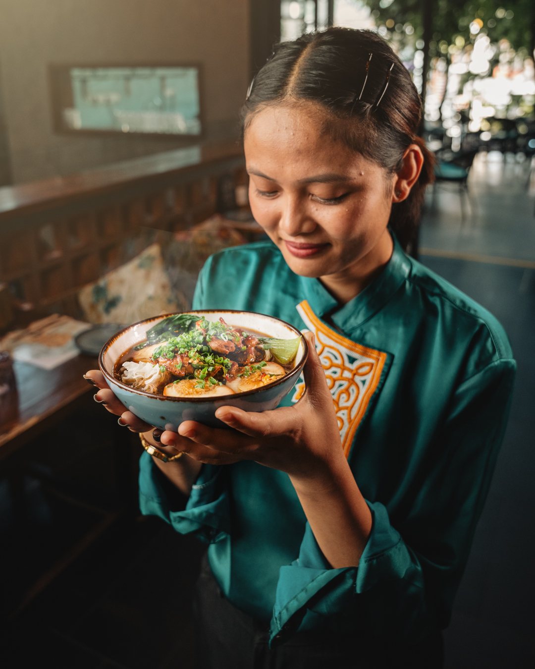 Khmer Kitchen server in a teal uniform holding a bowl of braised noodle soup